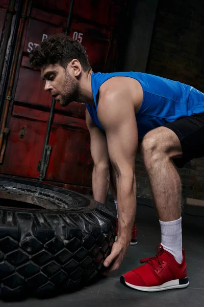 Uomo forte in abbigliamento sportivo sollevare pneumatico mentre si allena sulla strada della città di notte, fitness all'aperto — Foto stock