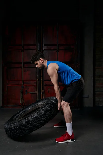 Longitud completa de hombre atlético fuerte levantar neumático mientras se entrena en la calle urbana por la noche - foto de stock