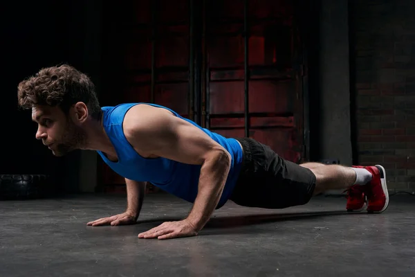 Concentrated man in blue tank top training in plank pose in darkness of night urban street — Stock Photo