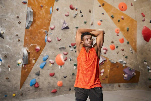 Спортивний афроамериканський чоловік з руками позаду голови дивиться з скелелазінням на фоні — стокове фото