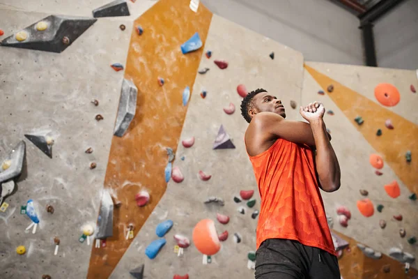 Atlético afro-americano homem em camisa laranja aquecimento com rock escalada parede pano de fundo, esporte — Fotografia de Stock