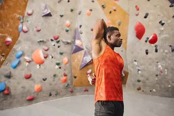 Homem atlético afro-americano em camisa laranja aquecendo com as mãos atrás das costas, conceito de escalada — Fotografia de Stock