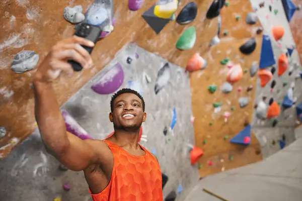 Happy african american man taking selfie and smiling cheerfully with climbing wall backdrop — Stock Photo