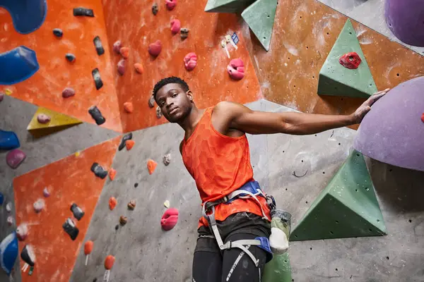 Athletic african american male model with alpine harness posing next to rock climbing wall — Stock Photo