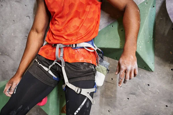 Abgeschnittene Ansicht eines muskulösen afrikanisch-amerikanischen Mannes mit orangefarbenem Hemd und Alpingeschirr, Bouldern — Stockfoto