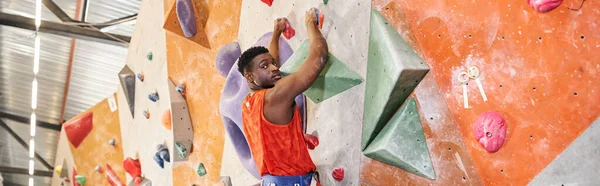 Bel homme afro-américain en chemise orange grimpant le mur et regardant la caméra, bannière — Photo de stock