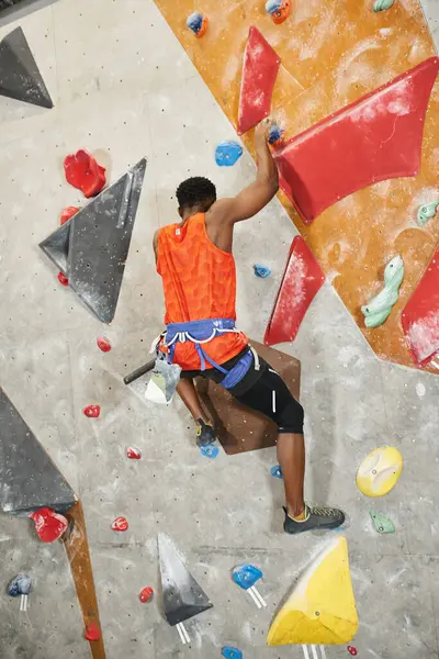 Vertical shot of young african american man climbing up rock wall, back view, bouldering concept — Stock Photo