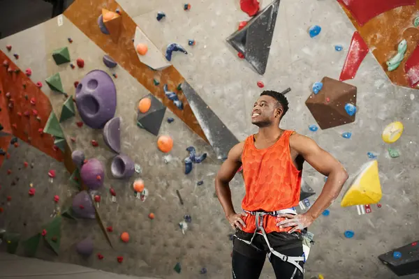 Young african american man posing in front of rock wall with hands on hips and smiling happily — Stock Photo