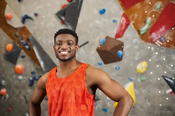 Красивый, веселый, африканский американец в оранжевой рубашке стоит рядом с каменной стеной и улыбается в камеру. — стоковое фото