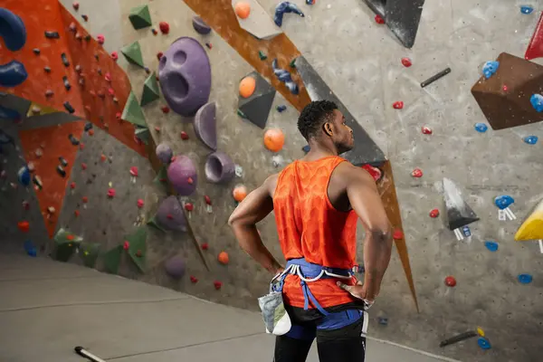 Rückansicht eines jungen afrikanisch-amerikanischen Mannes mit seinen Händen akimbo, der neben einer Kletterwand steht — Stockfoto