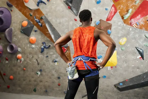 Muscular african american man in orange shirt posing next to rock bouldering wall, back view — Stock Photo