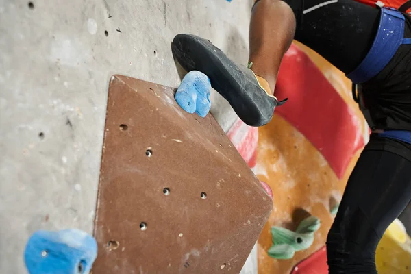 Vista ritagliata del piede dell'uomo americano africano sportivo sul masso sulla parete rocciosa rampicante, sportivo — Foto stock