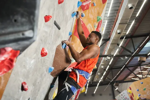 Young african american man with alpine harness posing in profile while climbing up bouldering wall — Stock Photo