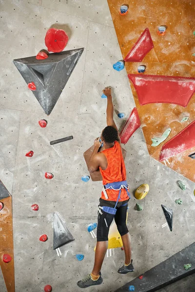 Vertical shot of sporty african american man hanging on his fingertips on rock wall, back view — Stock Photo