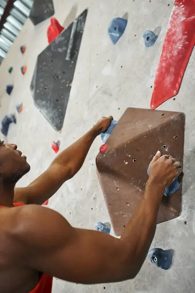 Vertikale Aufnahme eines sportlichen afrikanisch-amerikanischen Mannes, der an einem Felsbrocken an einer Kletterwand hängt, Sportler — Stockfoto