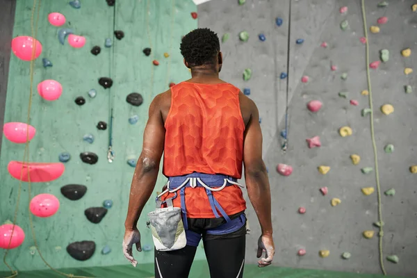 Back view of young african american man in orange shirt with alpine harness near bouldering wall — Stock Photo