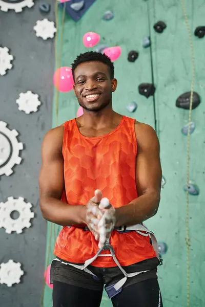 Tiro vertical de hombre afroamericano bien parecido usando tiza de gimnasio y sonriendo alegremente a la cámara - foto de stock