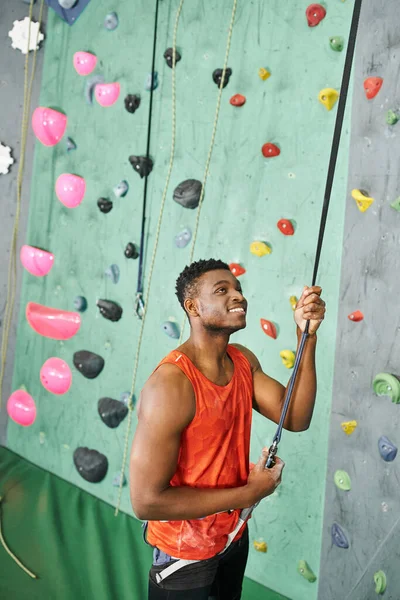 Tiro vertical de belo homem afro-americano sorridente usando corda de escalada, conceito de bouldering — Fotografia de Stock