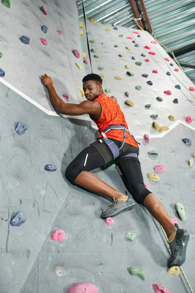 Schöner afrikanisch-amerikanischer Mann mit Sicherheitsseil und Klettergurt klettern und nach unten schauen — Stockfoto