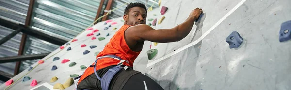 Homme afro-américain athlétique avec corde de sécurité grimpant et regardant vers le bas à la caméra, bannière — Photo de stock