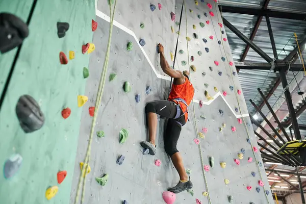 Fort athlète afro-américain avec harnais alpin escalade mur de roche saisissant sur les rochers — Photo de stock