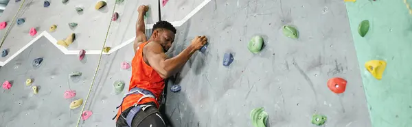 Muscular african american man with alpine harness and safety rope climbing up rock wall, banner — Stock Photo