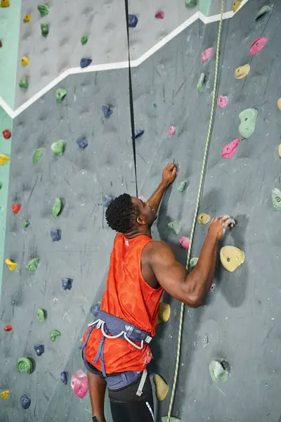 Vertical shot of african american man ascending up bouldering wall and looking up, sportsman — Stock Photo