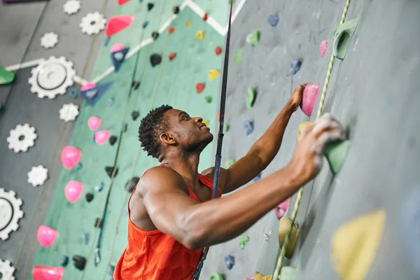 Joyeux homme afro-américain en chemise orange saisissant sur les rochers et regardant joyeusement vers le haut — Photo de stock