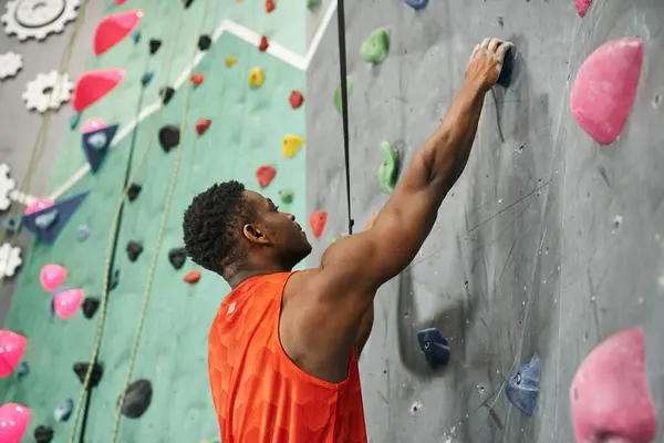 Bel homme sportif afro-américain saisissant sur les rochers tout en escaladant le mur, bloc — Photo de stock