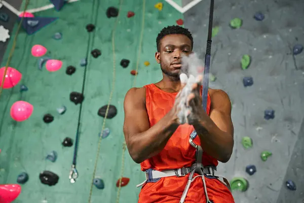 Handsome athletic african american man in orange shirt using gym chalk before ascending up rock wall — Stock Photo