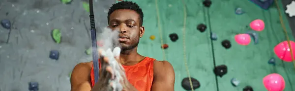 Sporty young african american man in orange shirt using gym chalk before climbing up wall, banner — Stock Photo