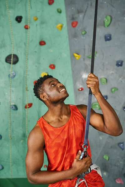 Vertical shot of cheerful young african american man holding on safety rope, bouldering concept — Stock Photo