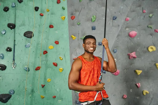 Alegre deportivo africano americano hombre en naranja camisa sonriendo alegremente a cámara, bouldering concepto - foto de stock