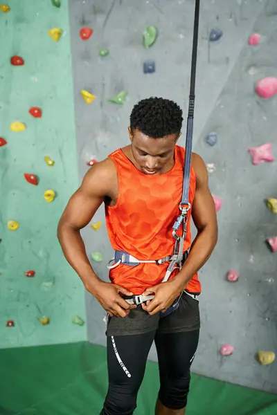 Vertical shot of sporty african american man checking on his alpine harness before climbing up wall — Stock Photo