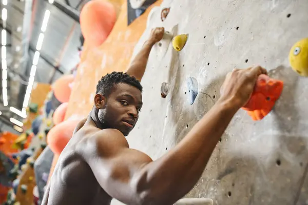 Good looking shirtless african american man gripping on boulders and looking straight at camera — Stock Photo