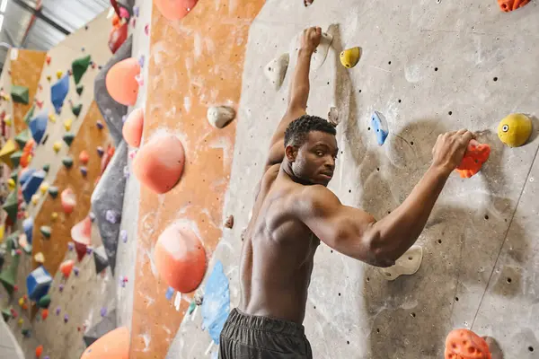 Bonito sem camisa afro-americano homem escalando até parede de rocha e olhando para a câmera, bouldering — Fotografia de Stock