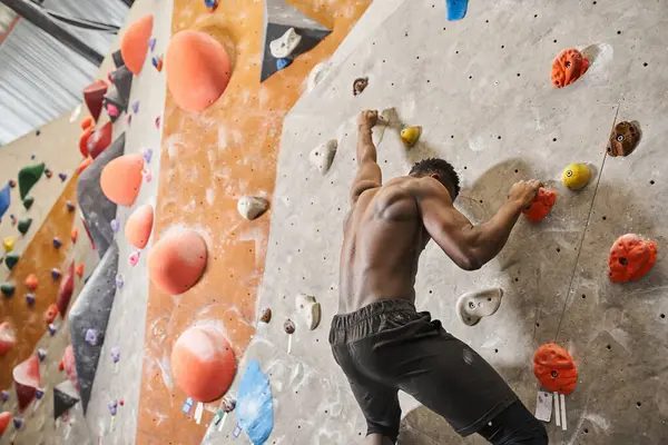 Good looking fit african american man with his shirt off climbing up rock wall and looking down — Stock Photo