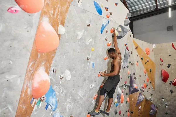 Athletic shirtless african american man in black pants climbing up rock wall without safety rope — Stock Photo