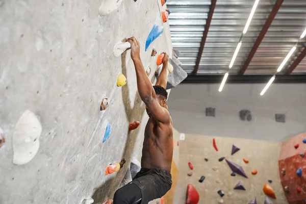 Muscular ajuste africano americano homem com sua camisa fora escalando até parede de rocha e olhando para baixo — Fotografia de Stock