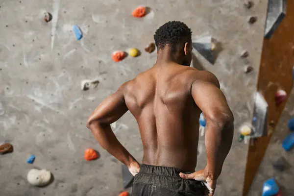 Back view of shirtless young african american man standing next to rock wall with hands on his hips — Stock Photo