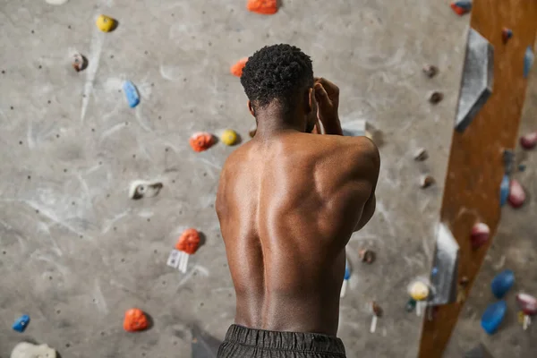 Добре виглядає топлес афроамериканський чоловік згинає м'язи, позуючи поруч зі стіною для скелелазіння — стокове фото