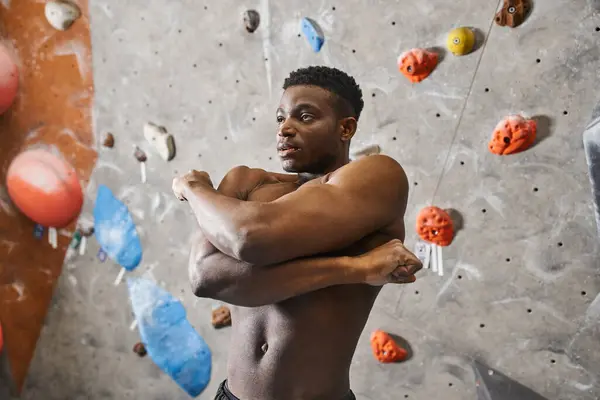 Bell'uomo afroamericano senza maglietta che posa vicino alla parete di arrampicata e allunga i muscoli — Foto stock