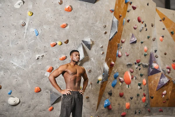 Bel homme musclé afro-américain posant seins nus à côté du mur d'escalade avec ses bras akimbo — Photo de stock
