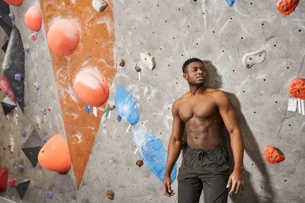 Good looking shirtless african american man posing right next to climbing wall, smiling slightly — Stock Photo
