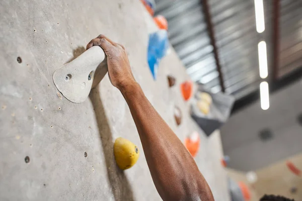 Cropped view of hand of sporty african american man gripping on boulders while climbing up wall — Stock Photo