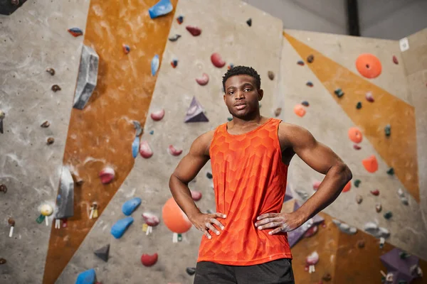 Gut aussehender junger afrikanisch-amerikanischer Mann in orangefarbenem Hemd posiert mit den Händen auf den Hüften und blickt in die Kamera — Stockfoto