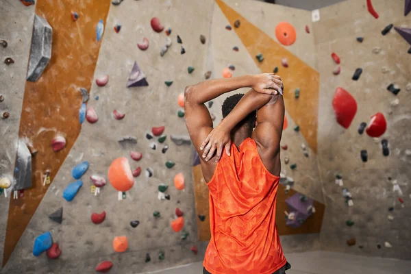 Visão traseira do jovem afro-americano com seus braços musculares atrás de sua cabeça ao lado da parede de escalada — Fotografia de Stock
