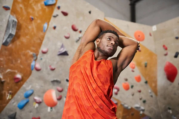 Good looking young african american man in orange shirt with his arms behind head, looking away — Stock Photo