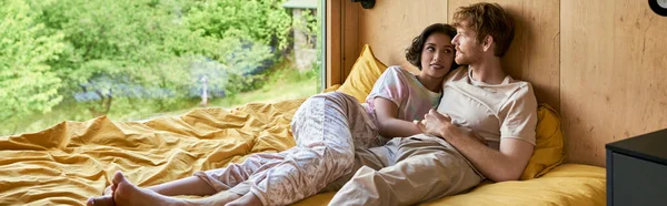 Rossa uomo sdraiato sul letto con allegra donna asiatica a guardare la finestra con vista naturale, banner — Foto stock