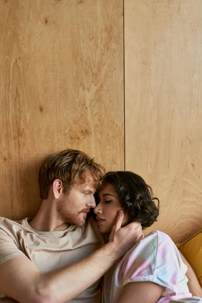 Casal interracial ter momento terno, ruiva homem tocando bochecha de mulher asiática e deitado na cama — Fotografia de Stock